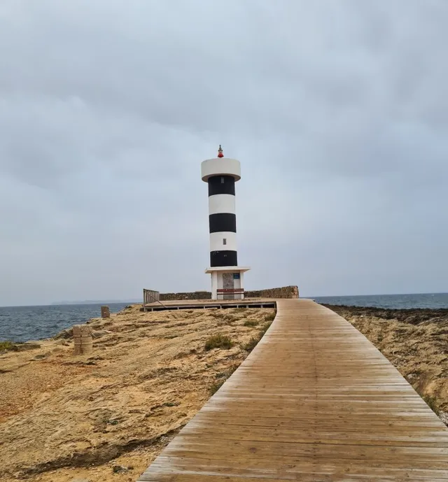 Ein Holzsteg führt zu einem Leuchtturm am Meer